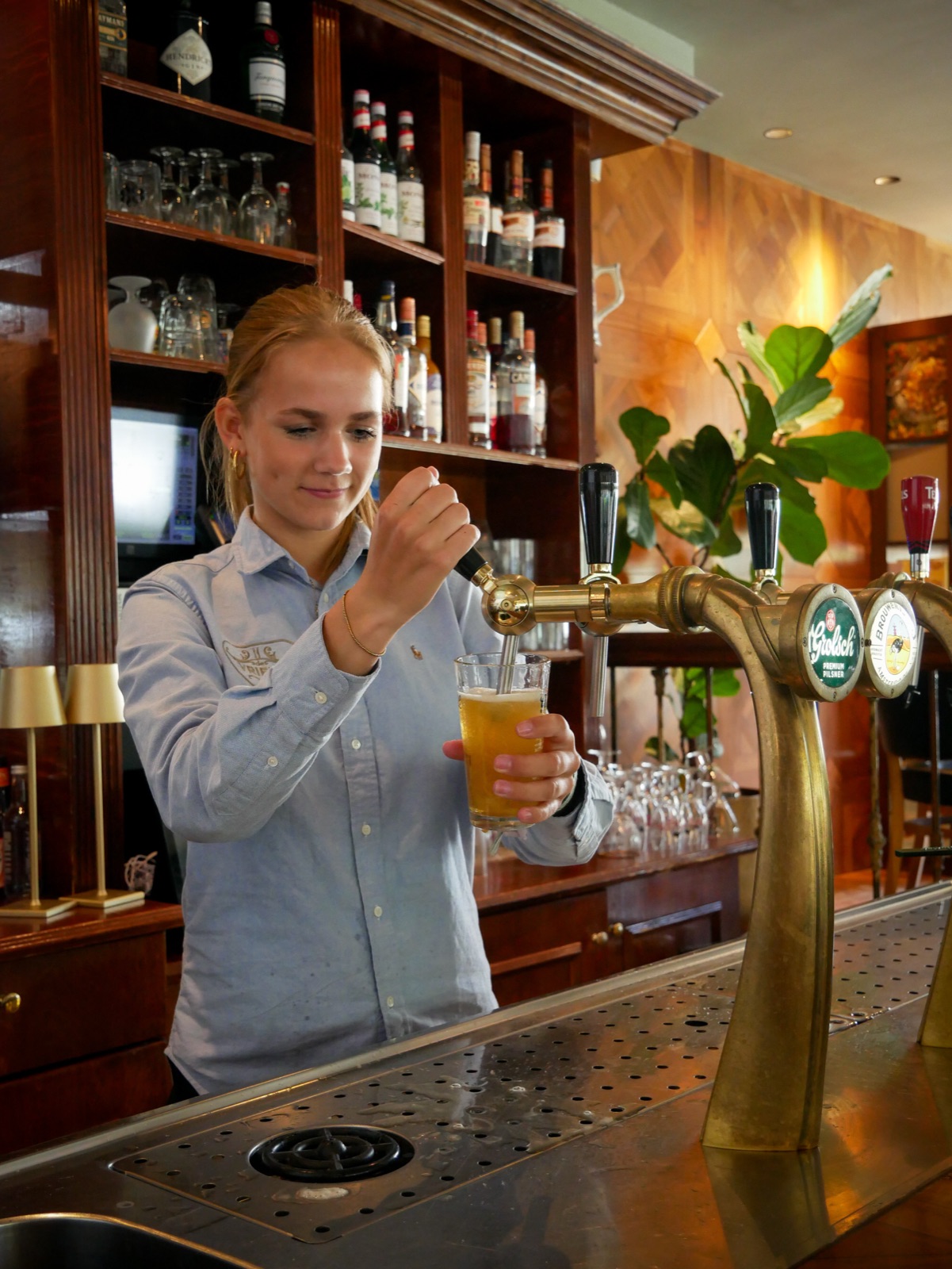 Een medewerker tapt een biertje aan de messing tapkranen van de klassieke houten bar