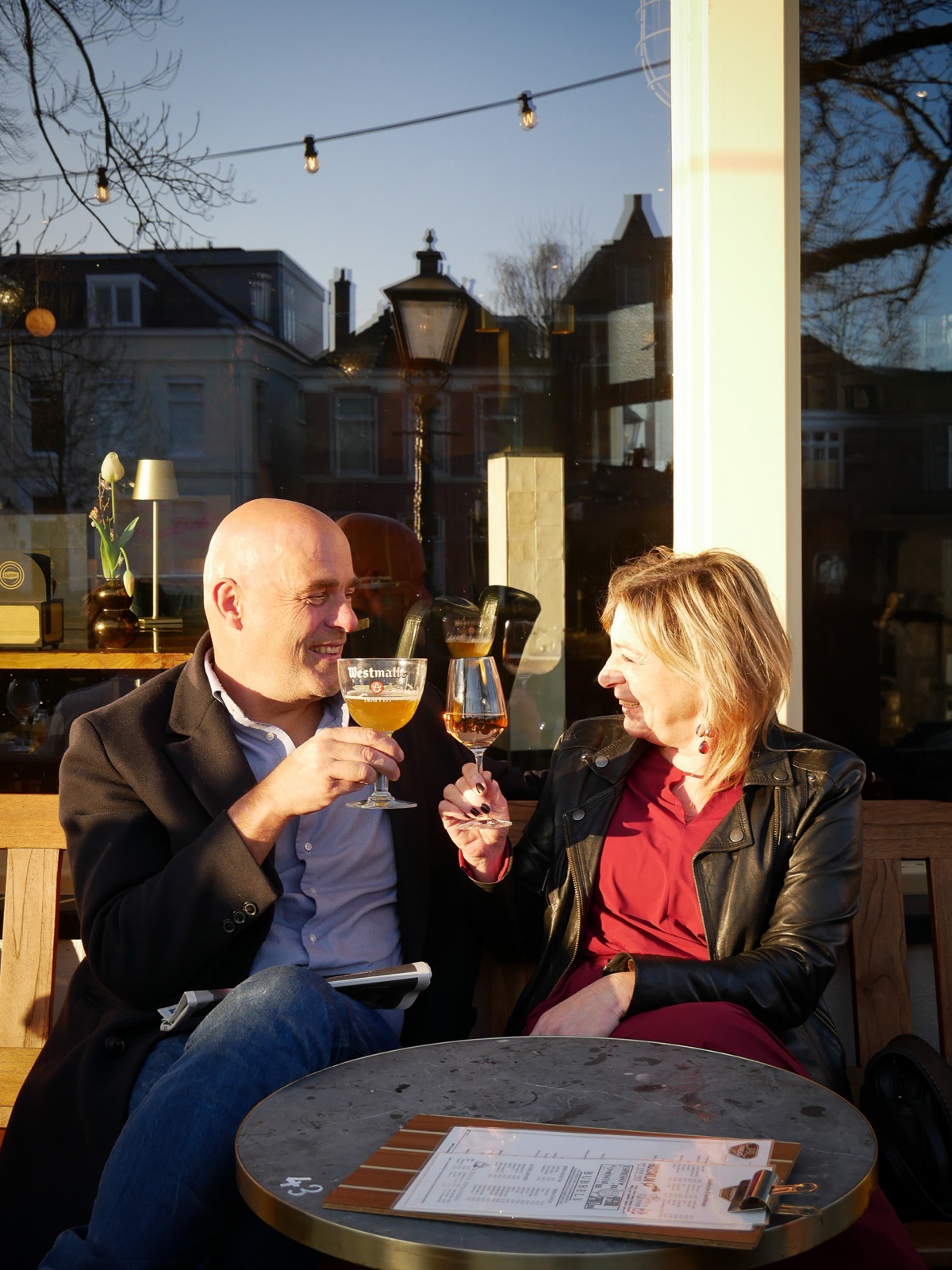 Een stel proost lachend met twee speciaalbieren op het terras van De Vriend in de avondzon