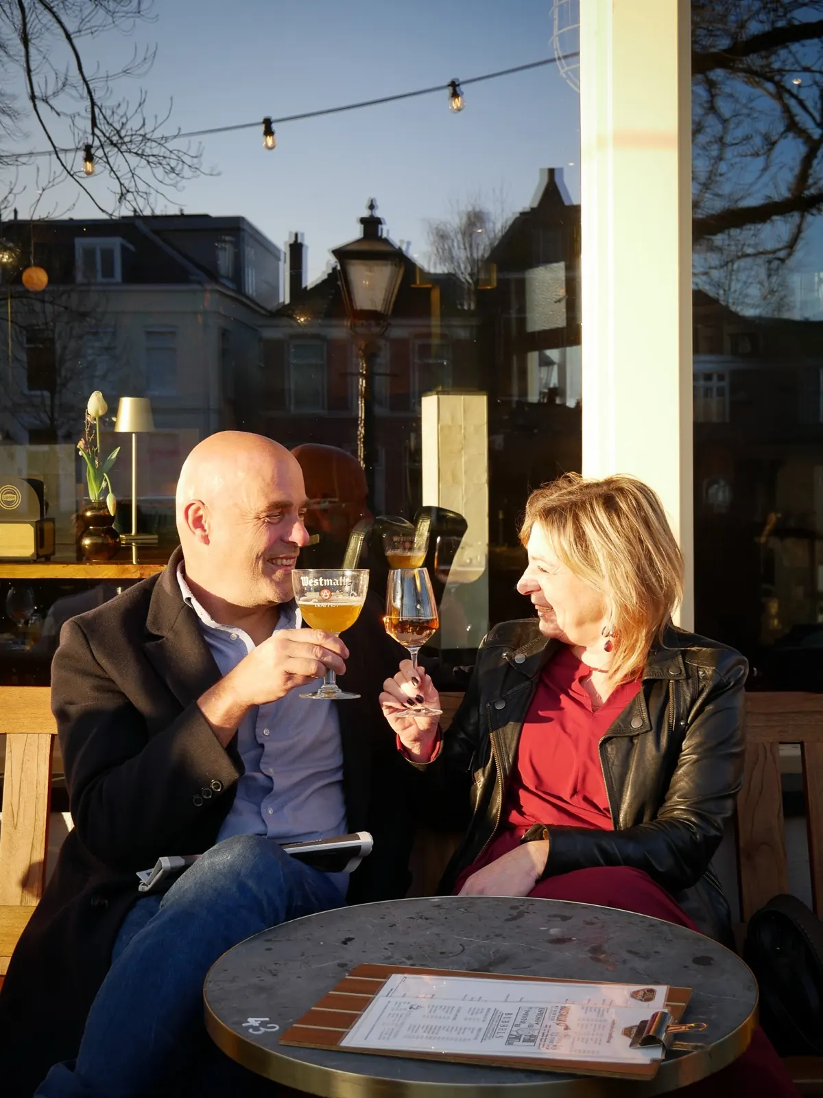 Een stel proost lachend met twee speciaalbieren op het terras van De Vriend in de avondzon