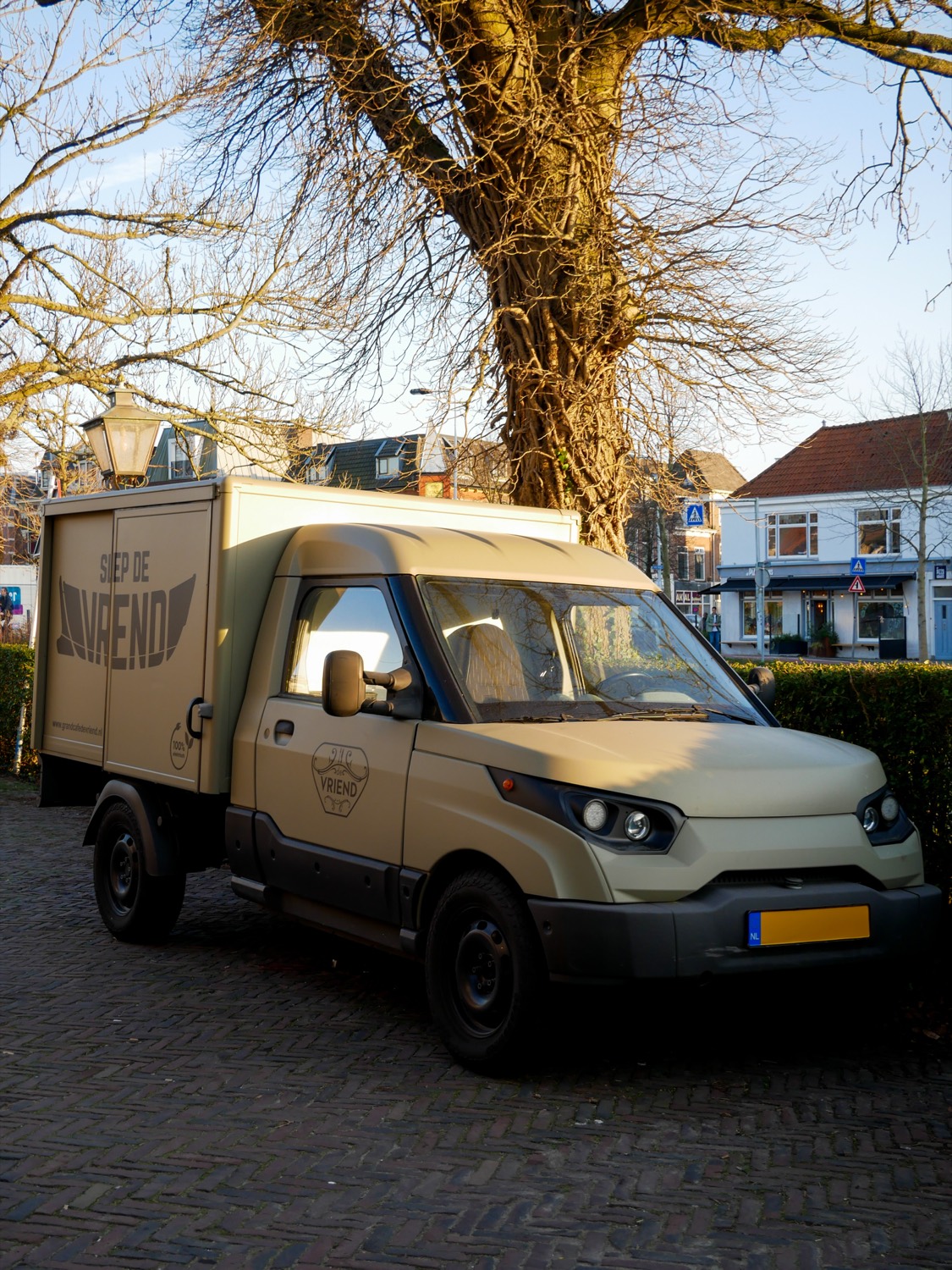 De olijfgroene cateringwagen van De Vriend, geparkeerd onder een grote boom in Leiden