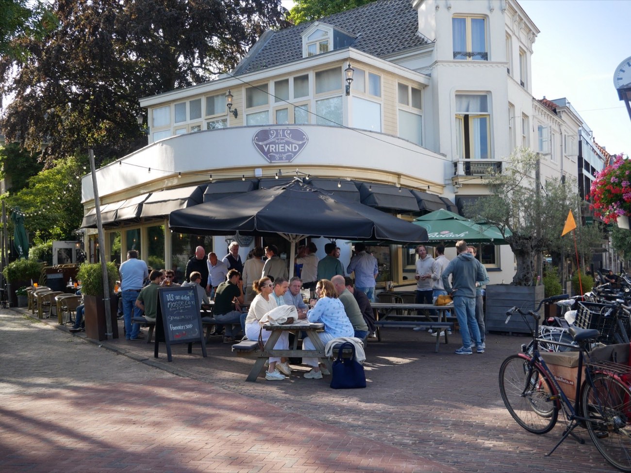 Het witte hoekpand van De Vriend met het terras vol gasten aan de lange tafels