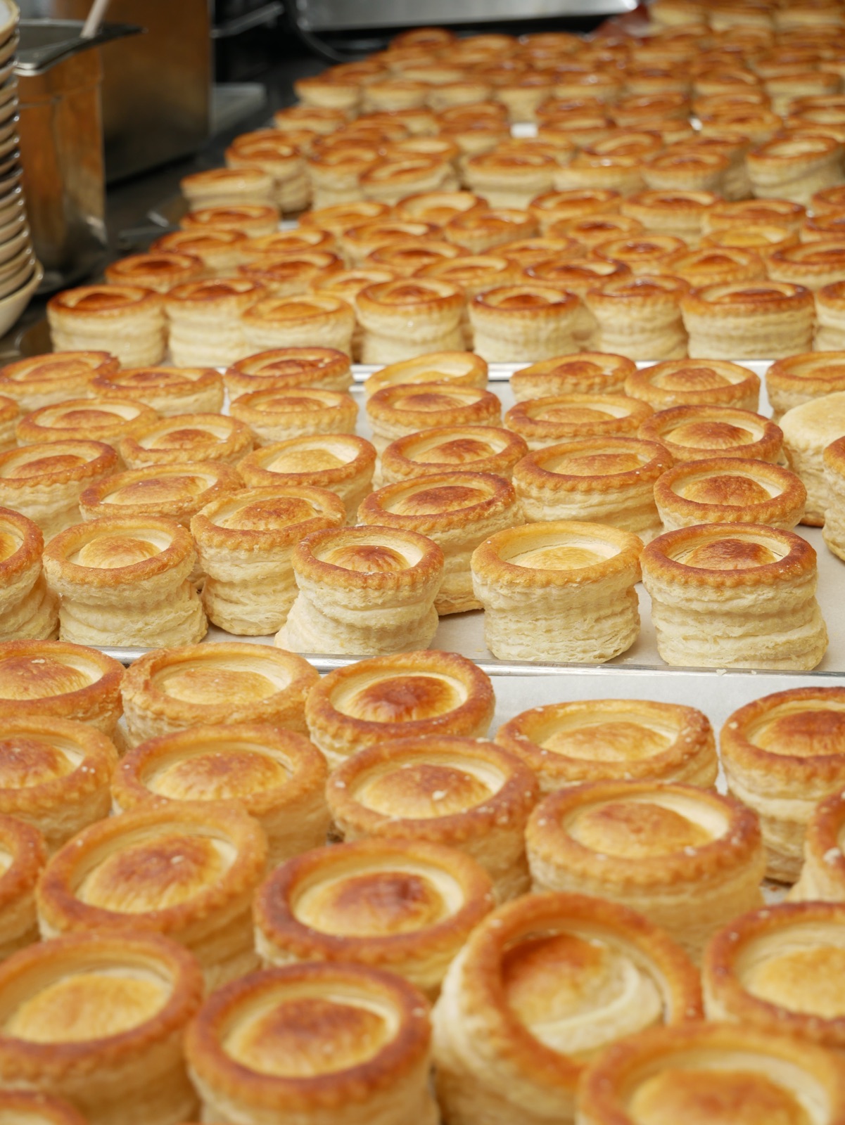 Rijen versgebakken pasteitjes op bakplaten in de keuken van De Vriend