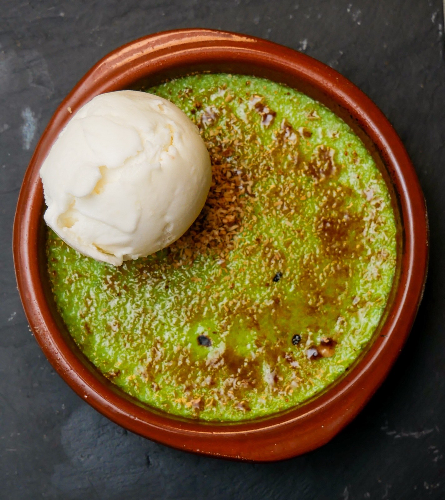 Pandan crème brûlée met een bol ijs in een aardewerken schaaltje
