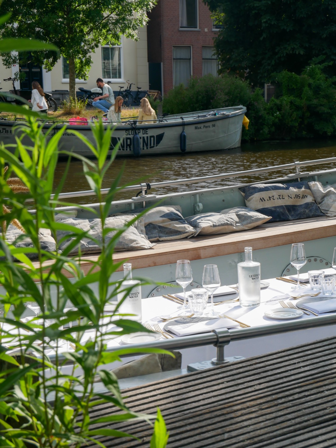 Gedekte tafel aan boord met wit linnen en goud bestek, met op de achtergrond de sloep van De Vriend op de singel
