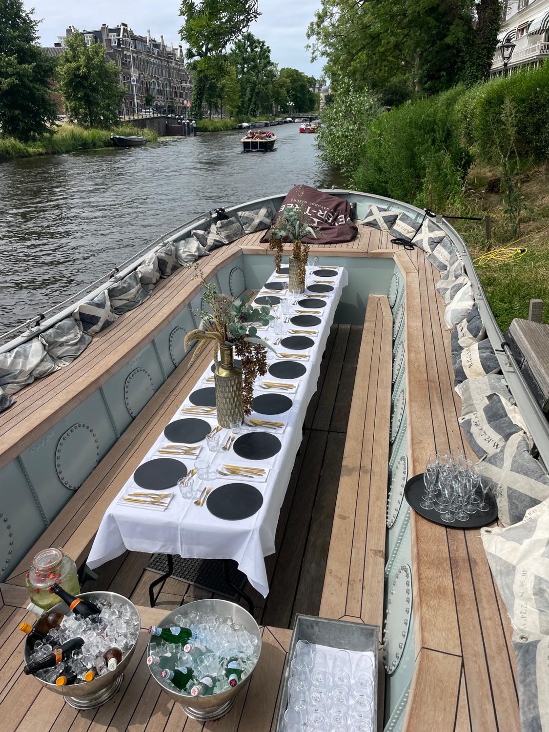 De volledig gedekte lange tafel aan boord van de sloep, met champagneglazen en koelers, varend over de singel