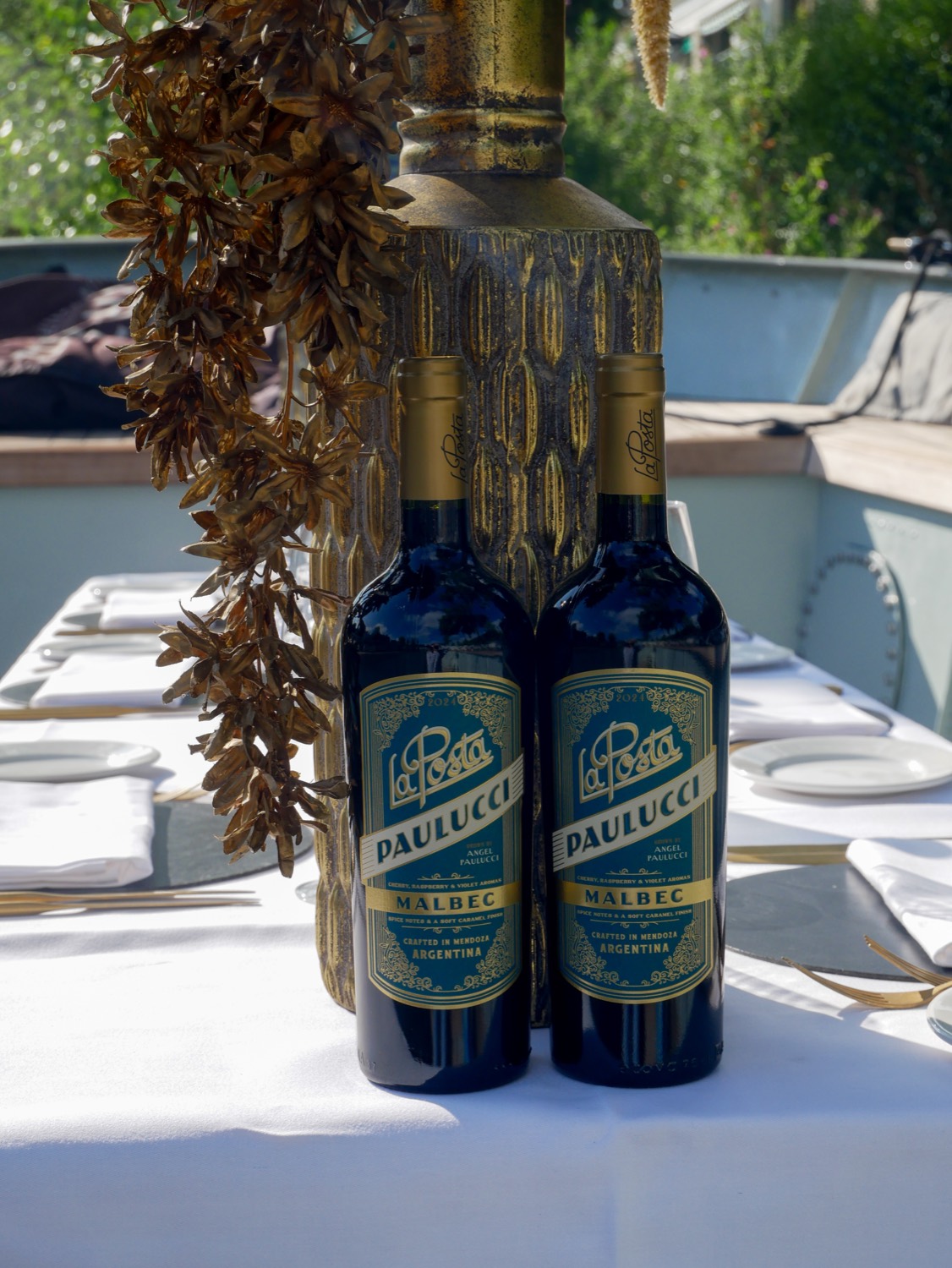 Twee flessen malbec op het witte tafellinnen aan boord, met een gouden vaas erachter