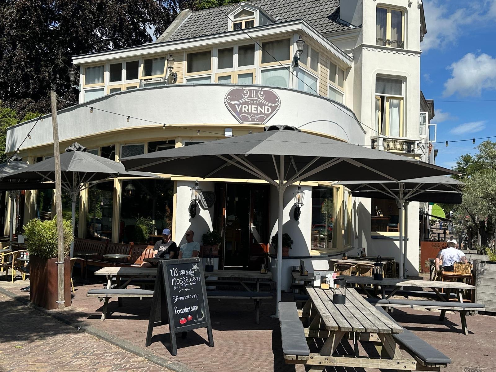 Het terras van De Vriend op een zonnige dag, met parasols, picknicktafels en het krijtbord met de vis van de dag
